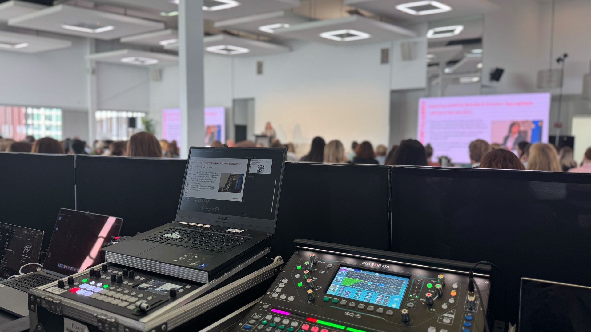Audio mixing desk and laptop at the back of a busy conference room