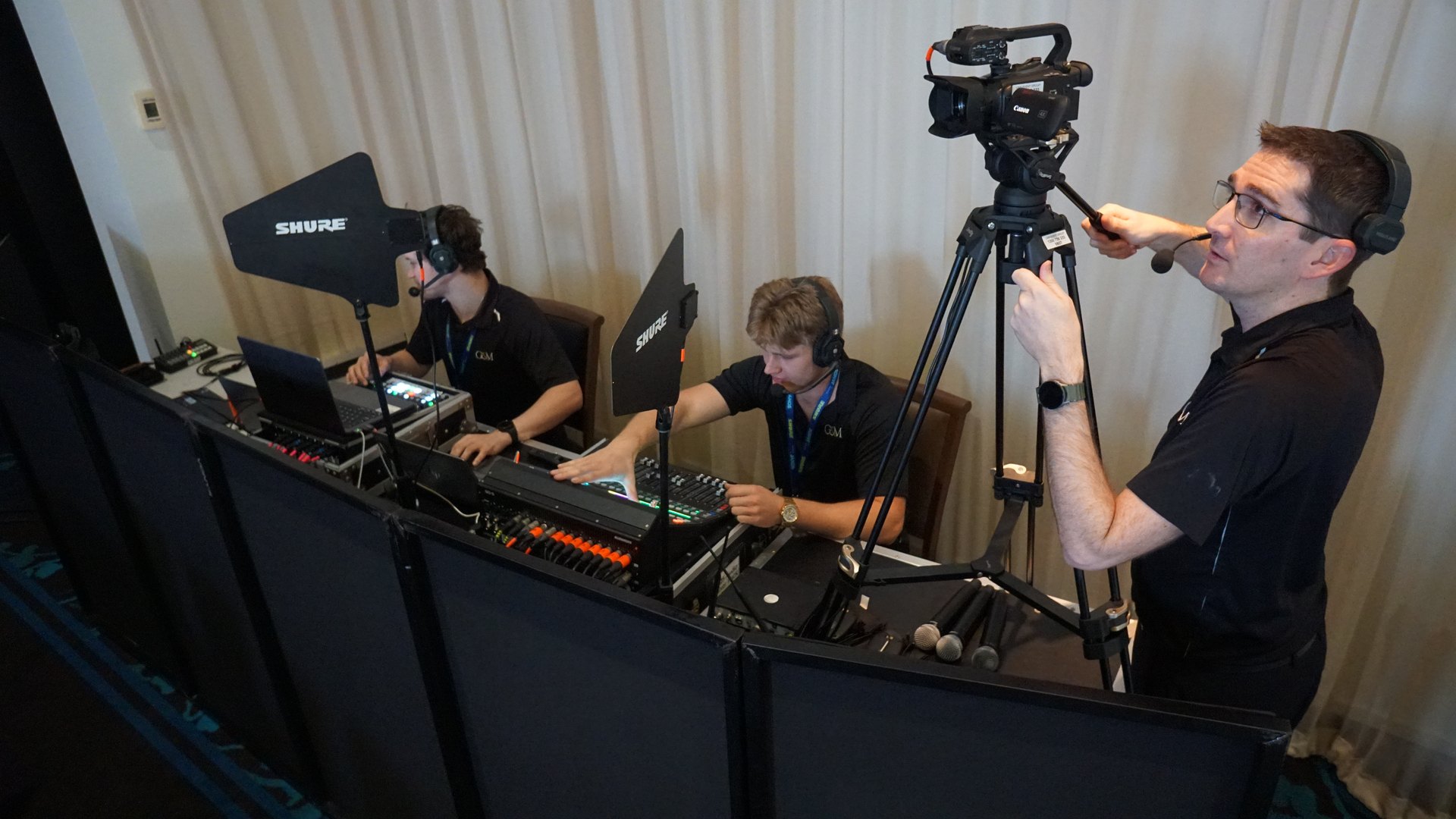 Camera operator filming beside technicians at the production desk during a conference