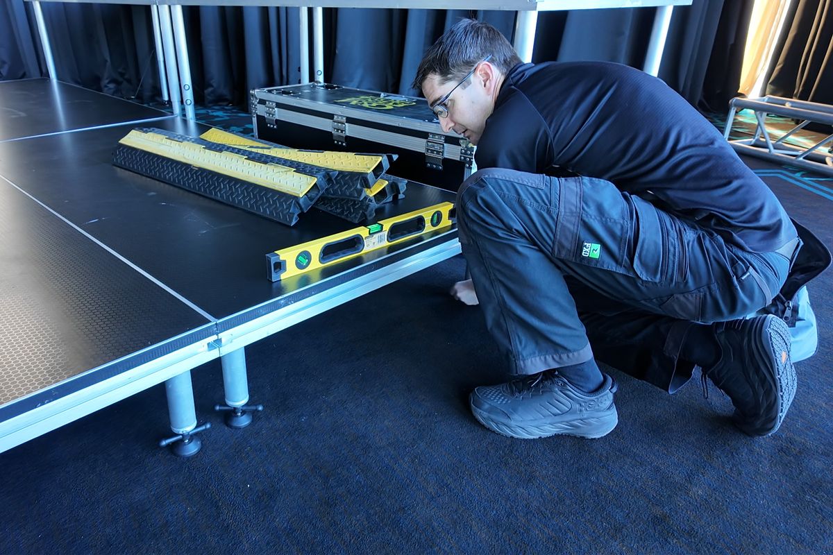 Crew member checking a stage deck is level with a spirit level during setup at Twin Towns