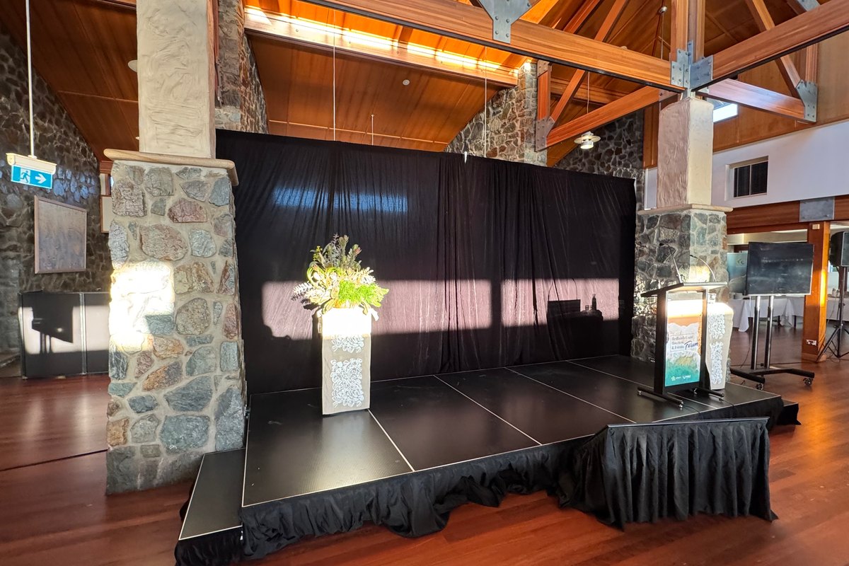 Stage with black drape backdrop, lectern, screen and floral arrangement